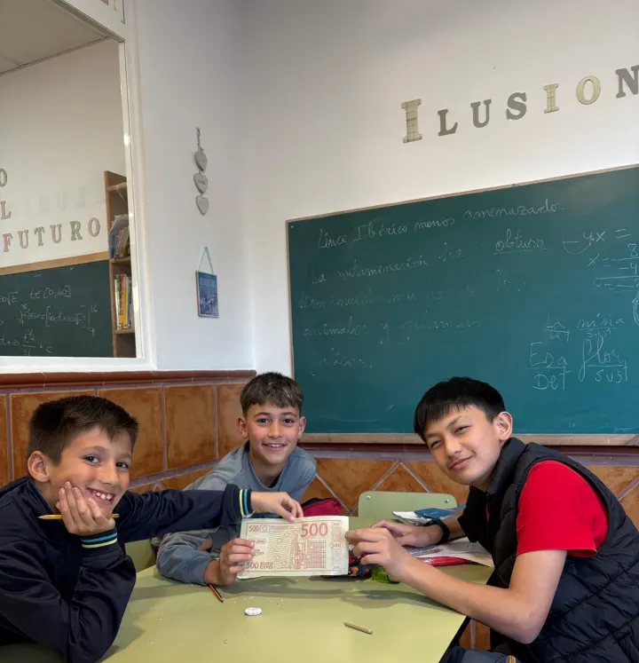 Tres alumnos sonriendo en una mesa de estudio de la academia